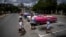 Turistas pasan frente a un estacionamiento lleno de autos clásicos estadounidenses que esperan a los clientes, en La Habana, Cuba, el 9 de julio de 2022. (Foto AP/Ramón Espinosa)