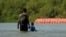 Migrantes caminan junto a grandes boyas que se utilizan como una barrera fronteriza flotante en el Río Grande, en Eagle Pass, Texas. (Foto AP/Eric Gay)